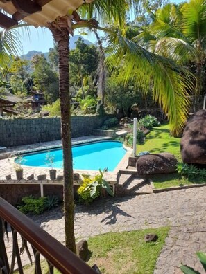 A swimming pool surrounded by lush greenery, a stone wall, and a stone pathway. - Retiro Canto da Mata (Ilhabela)