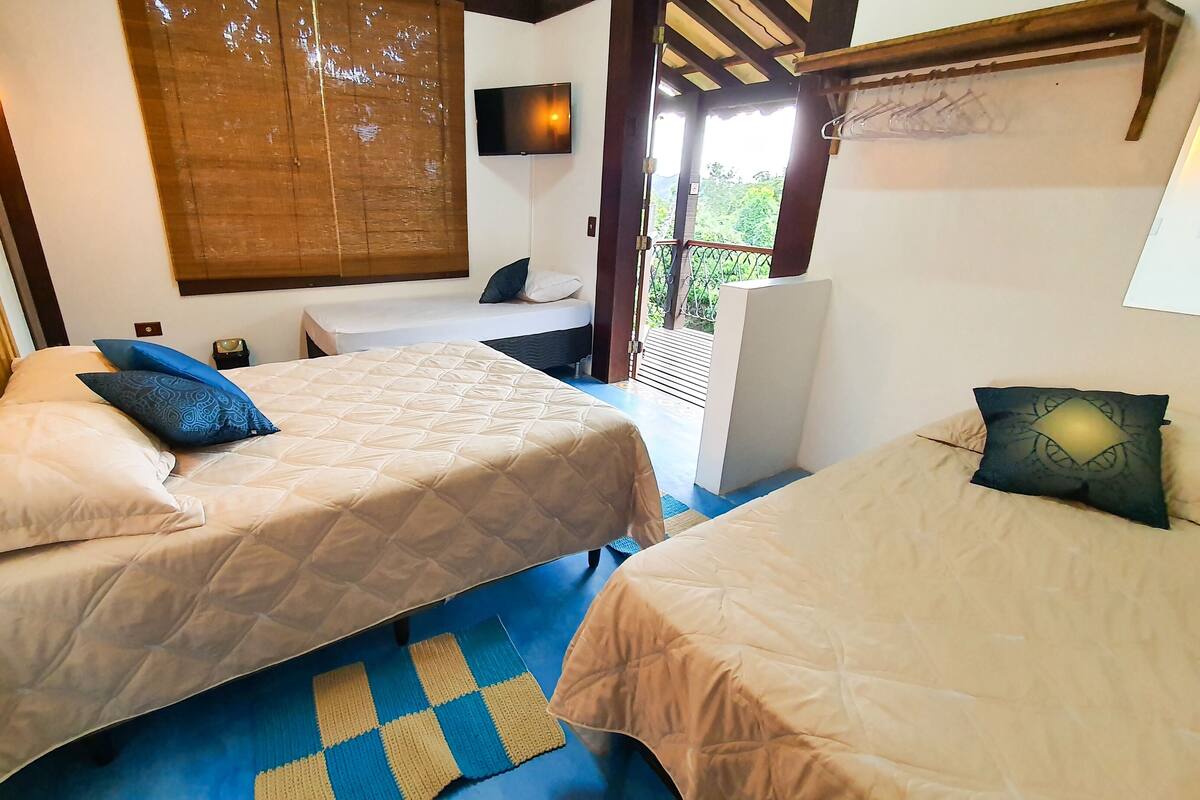 A room with two beds, a TV, and a window with a view of greenery.