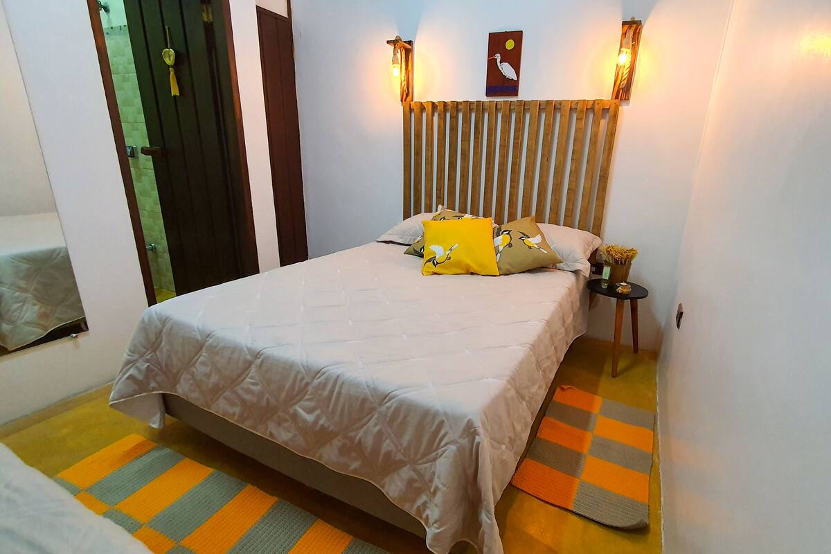A bedroom with a bed, pillows, a nightstand, a wall-mounted light, and a door.