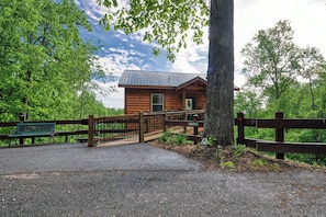 A wooden cabin with a metal roof, surrounded by a wooden fence and a paved path leading to it. - Jackalopia: Hot Tub, Firepit & Mountain Folklore!" (Gatlinburg)