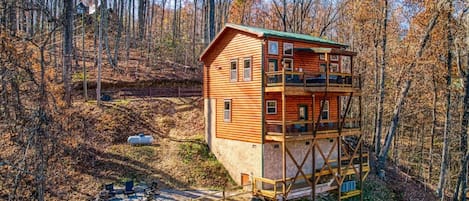 A multi-story log cabin with a balcony, surrounded by a forest.