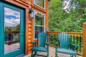 A wooden cabin with a deck, two Adirondack chairs, and a door with a window.
