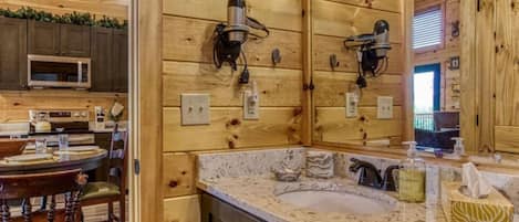 Un interior de madera con cocina, comedor y un baño con lavamanos y espejo.