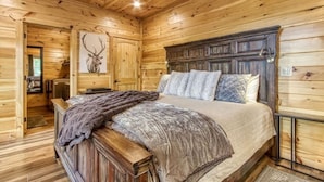 Quarto de cabana de madeira com cama, cabeceira, relógio fixado na parede e decoração com chifres de veado.