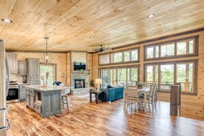 A spacious kitchen with wooden floors, a stone fireplace, and large windows.