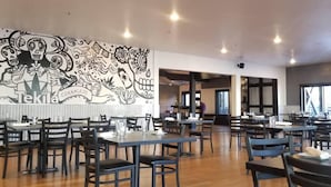 Ein Restaurant mit Tischen und Stühlen, einer Wandmalerei und Blick auf die Straße.