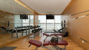 Ett gym med trägolv, utrustning för styrketräning och ett stort fönster med utsikt över staden.