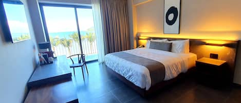 Une chambre d’hôtel moderne avec un grand lit, un bureau avec une chaise, une vue sur la mer et un tableau au mur.
