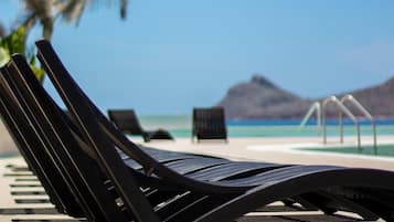 A black lounge chair on a beach with a clear blue sky and distant mountains.