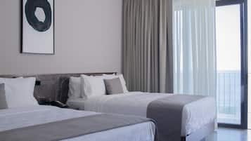 Habitación de hotel con dos camas, un ventanal con cortinas y vista al mar.