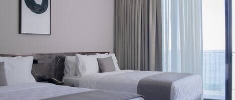 A hotel room with two beds, a large window with curtains, and a view of the sea.