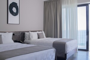 Habitación de hotel con dos camas, un ventanal con cortinas y vista al mar.