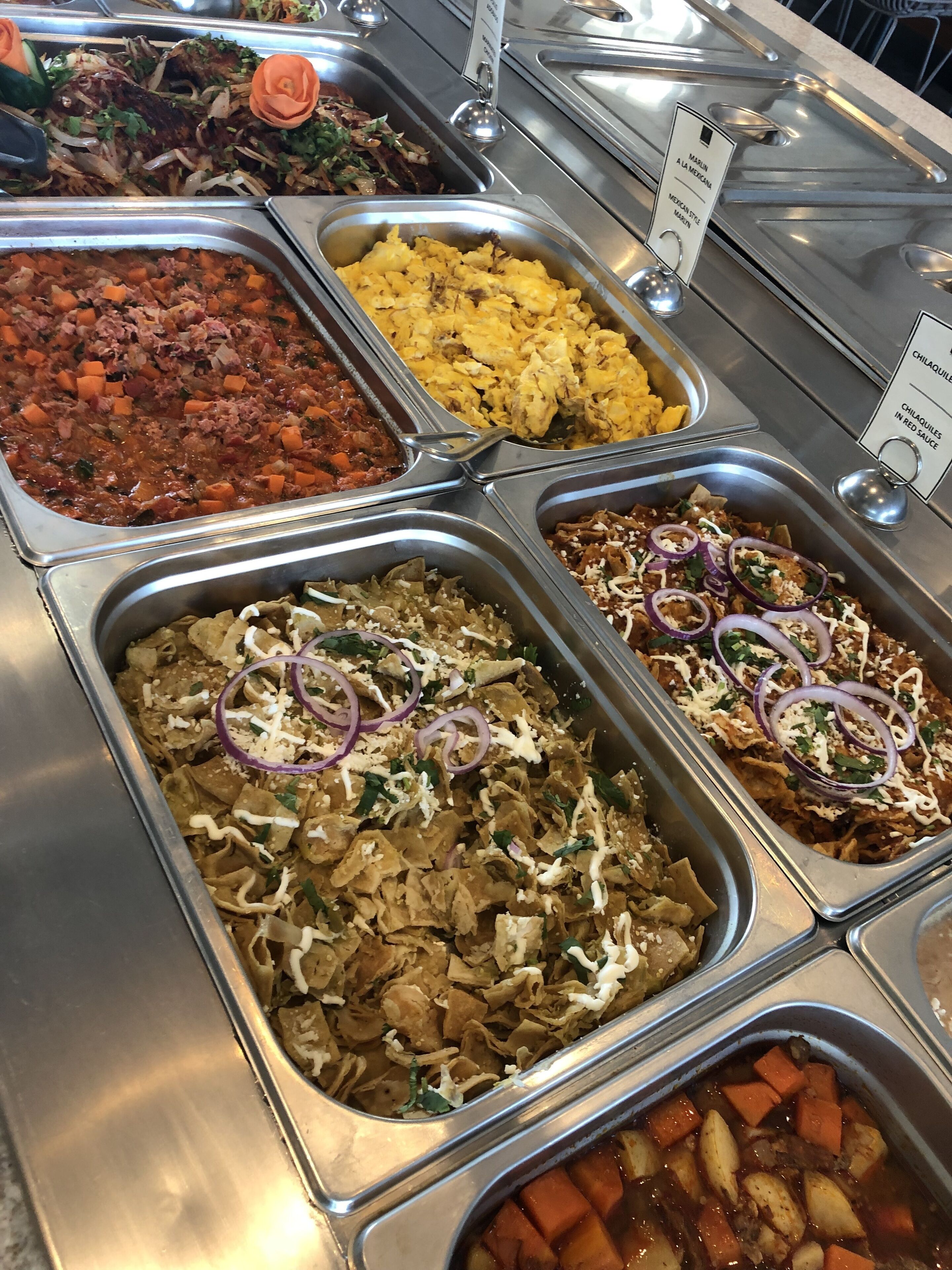 Un buffet proposant divers plats, notamment de la viande marinée, des œufs brouillés et une salade de haricots.