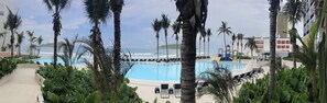 Ein Poolbereich mit Liegestühlen, Palmen und Blick aufs Meer.