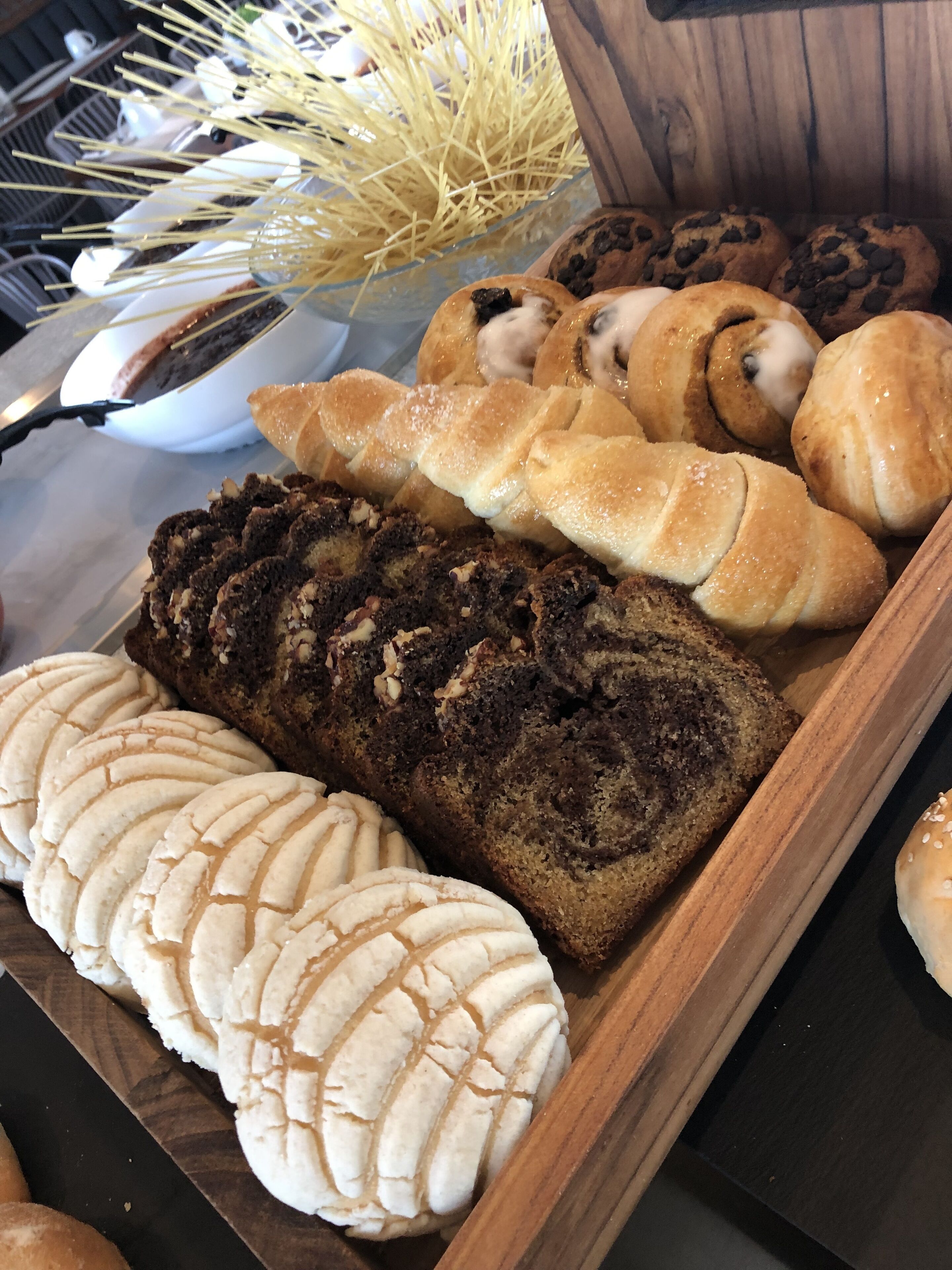 Diversa variedad de productos horneados, como pan, pasteles y galletas, expuestos en una bandeja de madera.