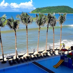 Relax by the ocean with a clear view of the lush hillside, surrounded by palm trees and lounge chairs.