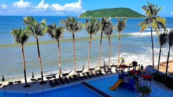 A resort pool with lounge chairs, palm trees, and a view of the ocean.