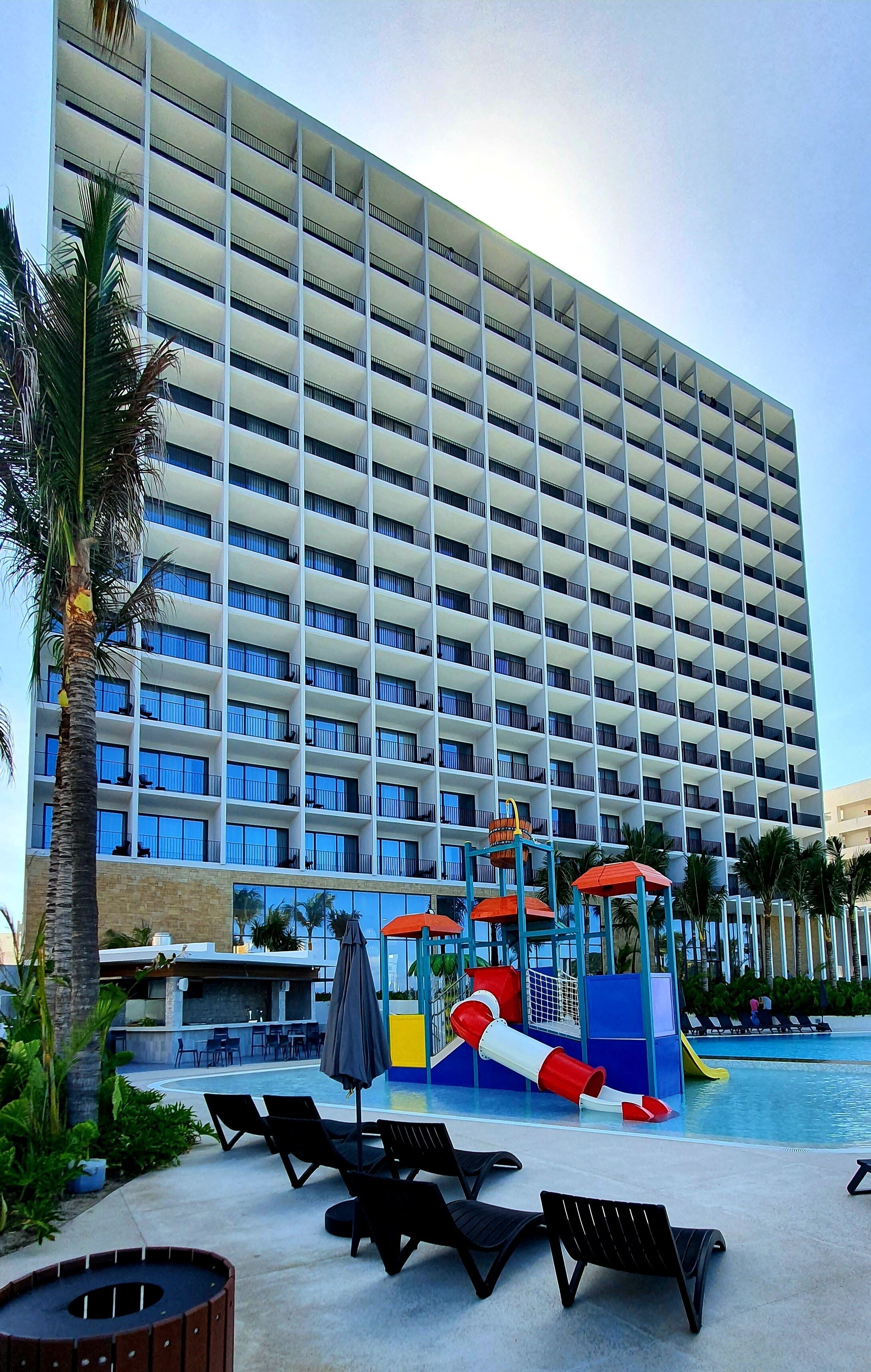 Un hôtel doté d’un grand espace piscine, comprenant un toboggan aquatique et des chaises longues.