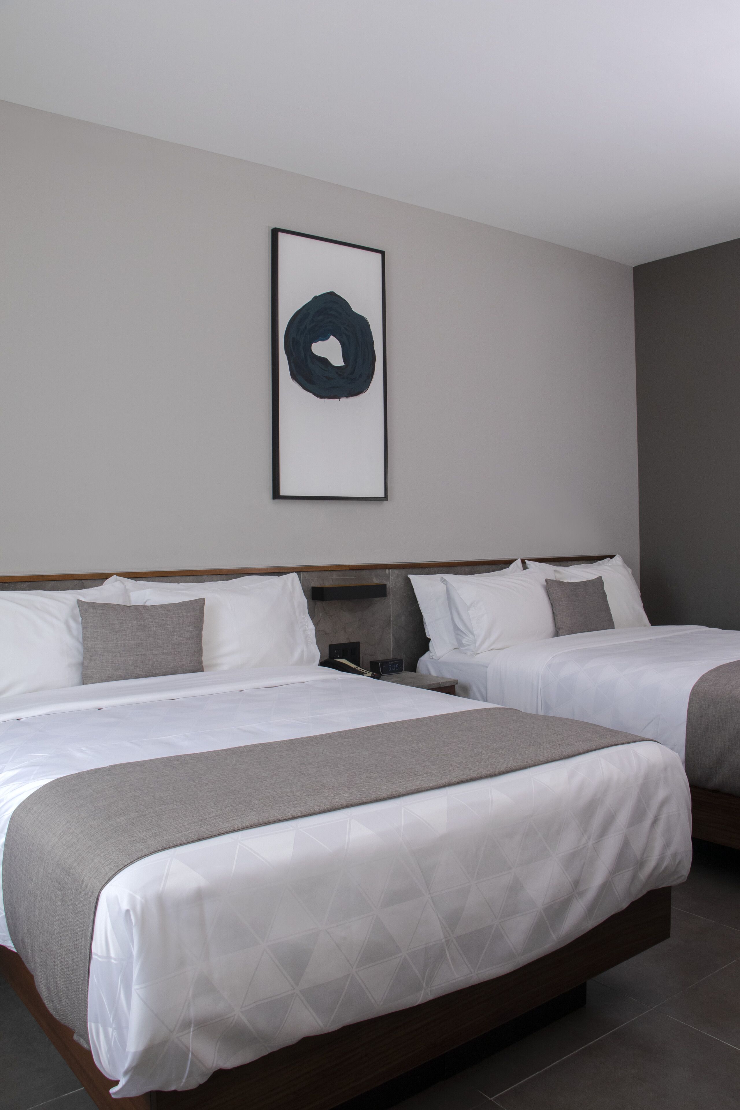 A hotel room with two beds, a framed artwork on the wall, and a neutral color scheme.