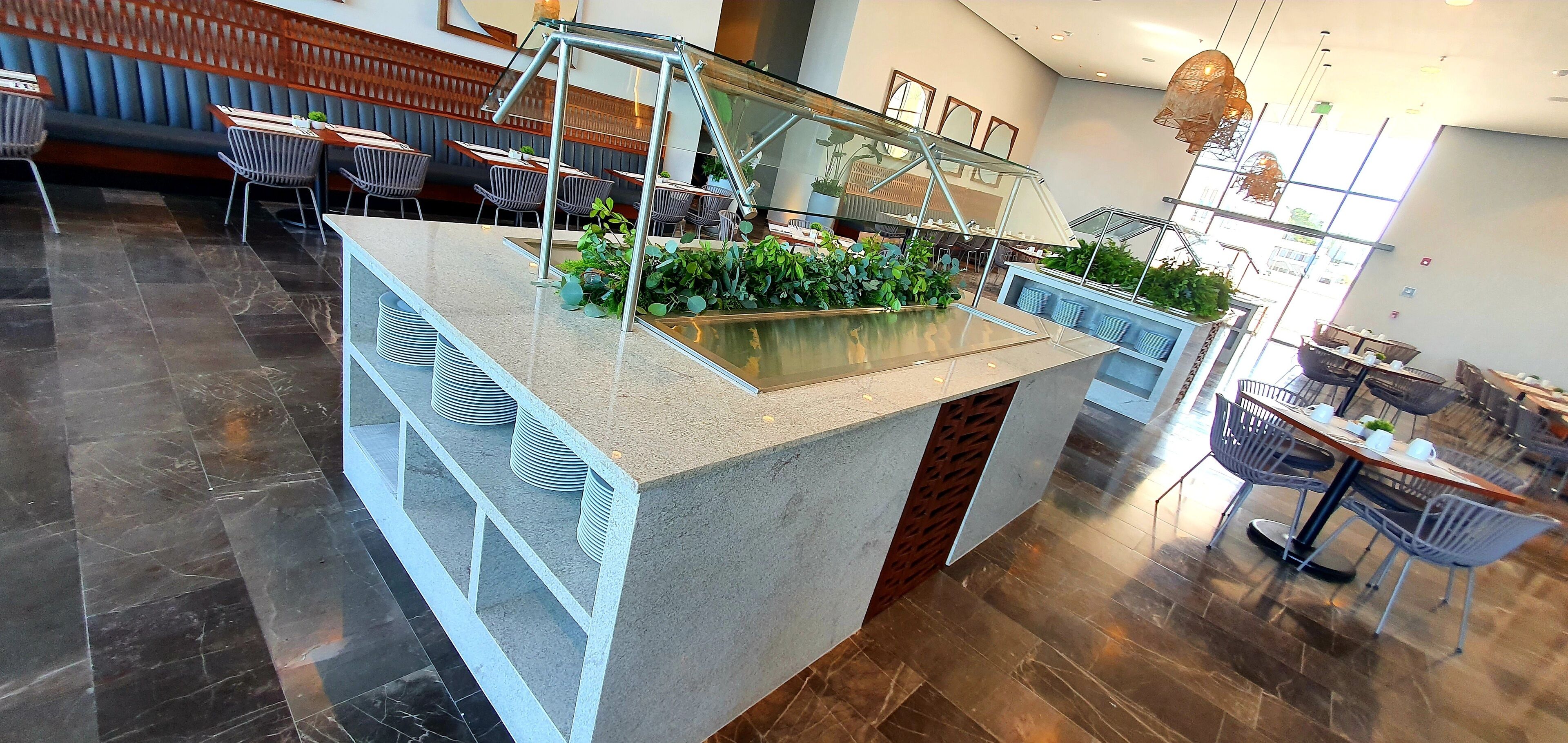 A modern restaurant with a central island, seating areas, and a staircase.