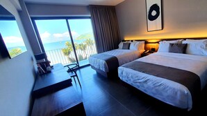 Ein Hotelzimmer mit zwei Betten, einem Schreibtisch und Blick auf den Ozean.
