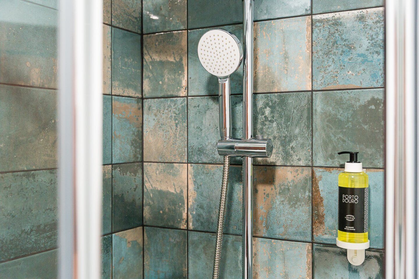 A shower area with a handheld showerhead and a bottle of Porto Douro shampoo.
