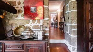 A stone-walled hallway with rustic decor, including a wooden cabinet and a painting. - Casa Museu Rural Hotel (Cinfães)