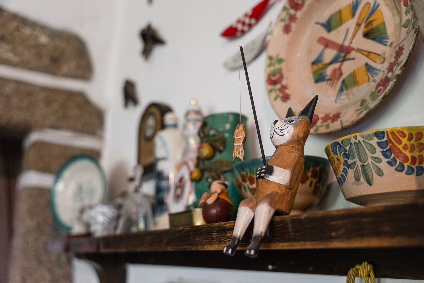 Una estant amb diversos objectes decoratius, com una figura de gat de ceràmica, un rellotge i un plat amb un disseny floral.