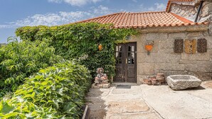 A stone building with a tiled roof, a wooden door, and a small garden area with plants and a stone bench. - Casa Museu da Geada: Room 2 (Cinfães)