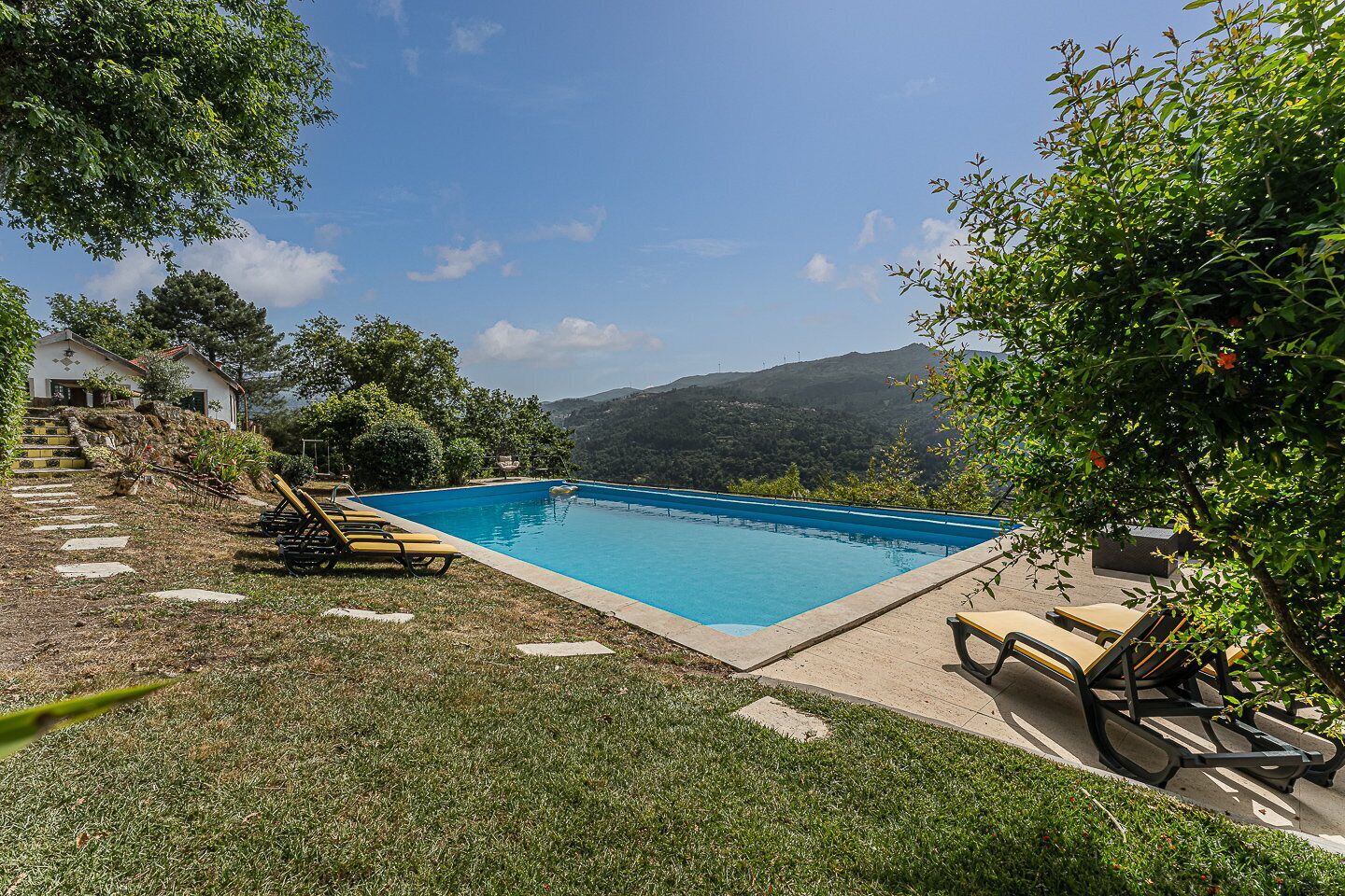 Une piscine rectangulaire à l’eau d’un bleu limpide, entourée d’une pelouse où sont disposés quelques chaises longues.
