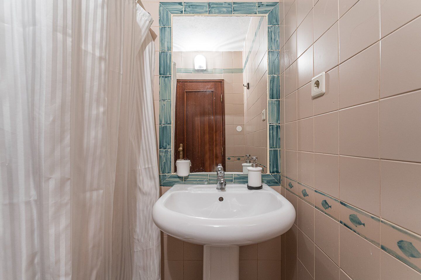 A bathroom with a white sink, a mirror with a blue frame, and a wooden door.
