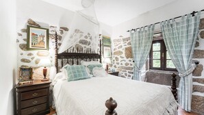 A bedroom with a stone wall, a bed with a canopy, a nightstand, and a window with curtains. - Casa Museu da Geada: Room 2 (Cinfães)