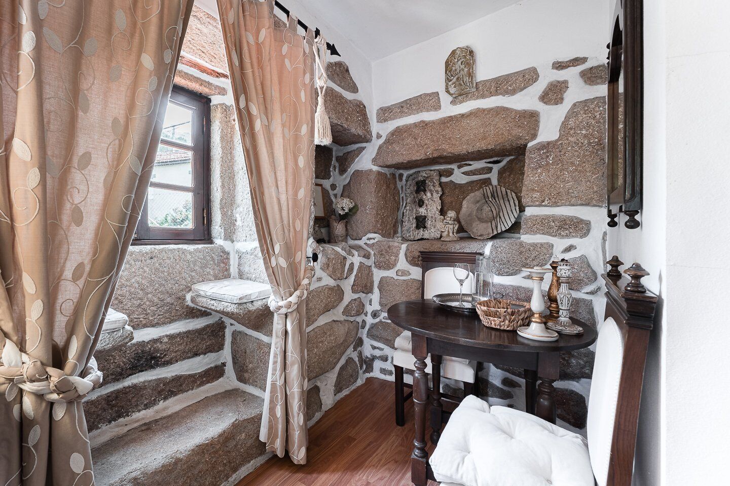 Une salle de bain rustique aux murs de pierre, dotée d’une fenêtre, d’un lavabo et d’une table ronde agrémentée d’objets décoratifs.