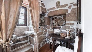 Une salle de bain rustique aux murs de pierre, dotée d’une fenêtre, d’un lavabo et d’une table ronde agrémentée d’objets décoratifs.