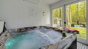 A hot tub with a view of a forest through large windows.
