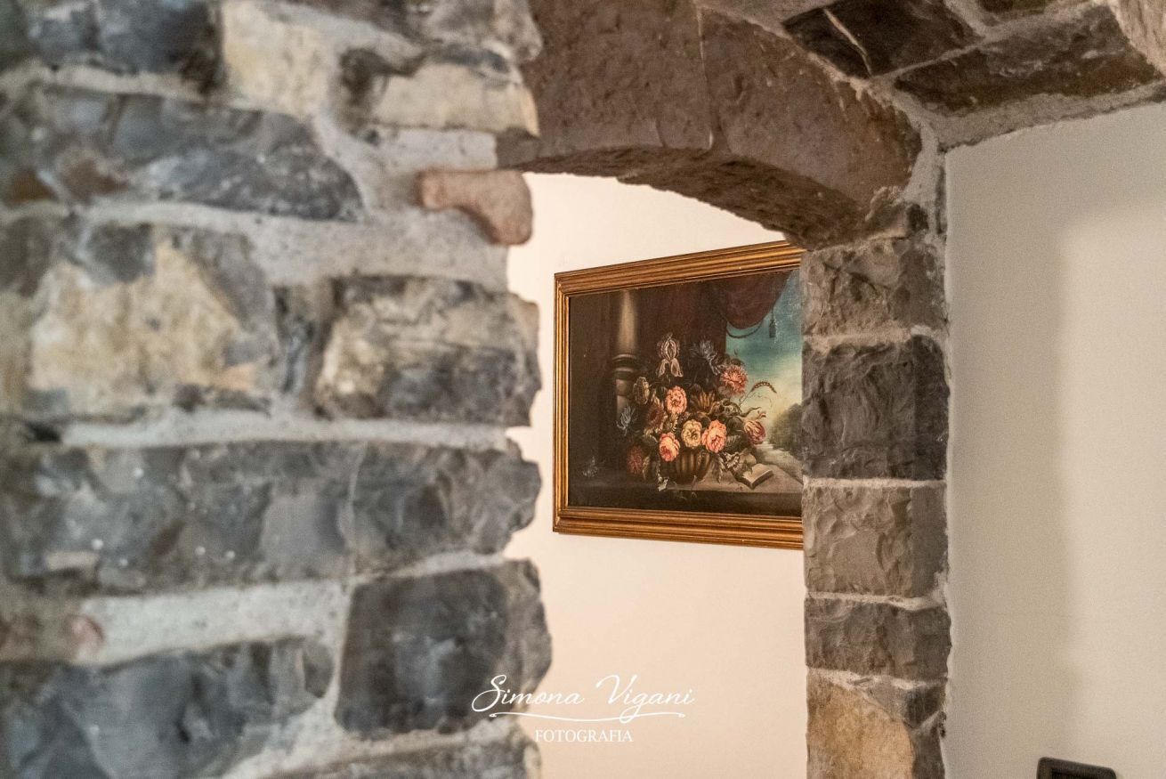 Un arc en pierre mène à une pièce dont le mur est orné d’un tableau floral encadré.