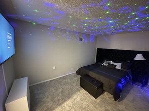 Relax in this serene bedroom with a large bed, flat-screen TV, and starry night sky ceiling projection.
