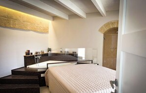 A modern bathroom with a large bathtub, a separate shower area, and a bed with a beige quilted bedspread.