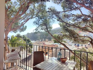 A balcony with a table, chairs, and a railing overlooking a coastal town with buildings and trees. - Stunning & Intimate views. Terrace + Rooftop. Wifi (Tamariu)