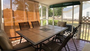 Een overdekt terras met een tafel en stoelen, een beschut gedeelte en uitzicht op de omgeving.