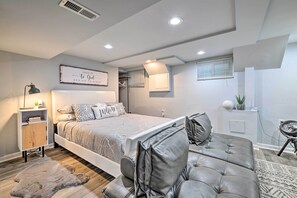 Quarto moderno com uma cama grande, um sofá de couro cinzento, uma mesa de cabeceira com abajur e uma estante fixada na parede.