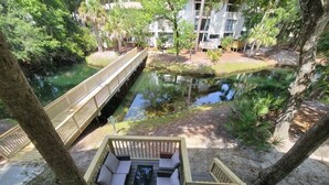 Une terrasse en bois avec un canapé et une petite table, donnant sur un étang et un pont.