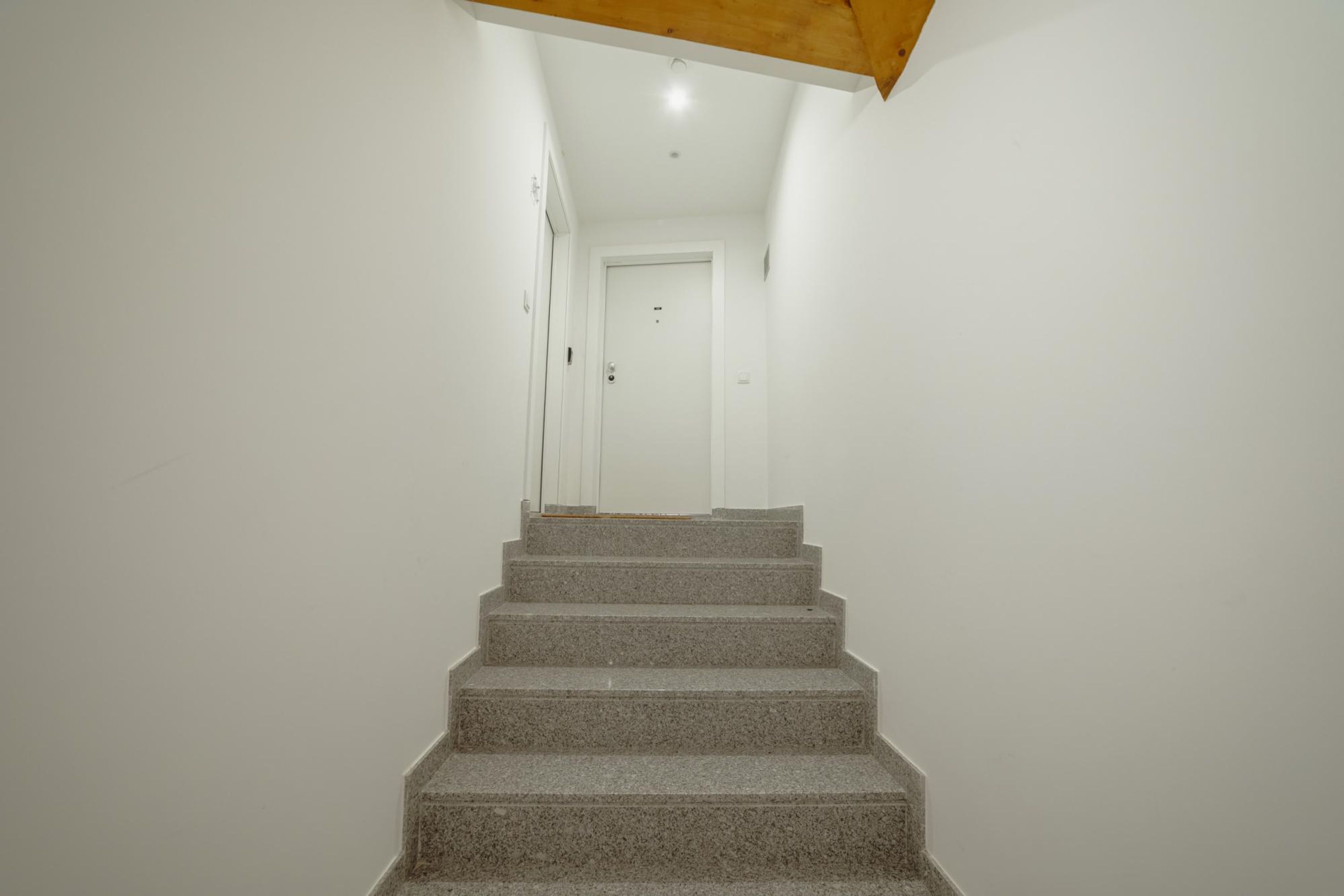 A staircase leading to a door in a room with white walls and a wooden ceiling beam.