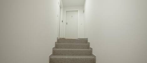 A staircase leading to a door in a room with white walls and a wooden ceiling beam.