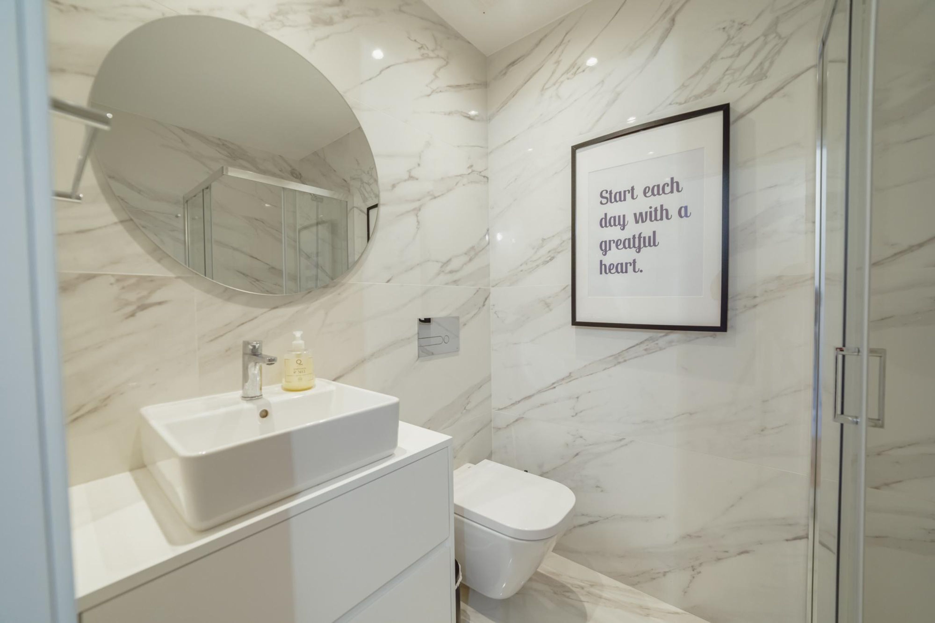Un baño moderno con pared de mármol, un lavabo, un inodoro y una cita inspiradora enmarcada.