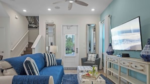 A living room with a blue sofa, a coffee table with a tray, a TV, and a staircase. - Get Happy (Kissimmee)