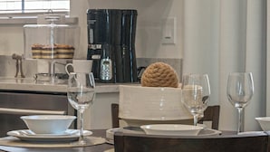 A dining area with a table set for two, including plates, bowls, and wine glasses. A coffee maker and a cake are visible in the background. - Get Happy (Kissimmee)