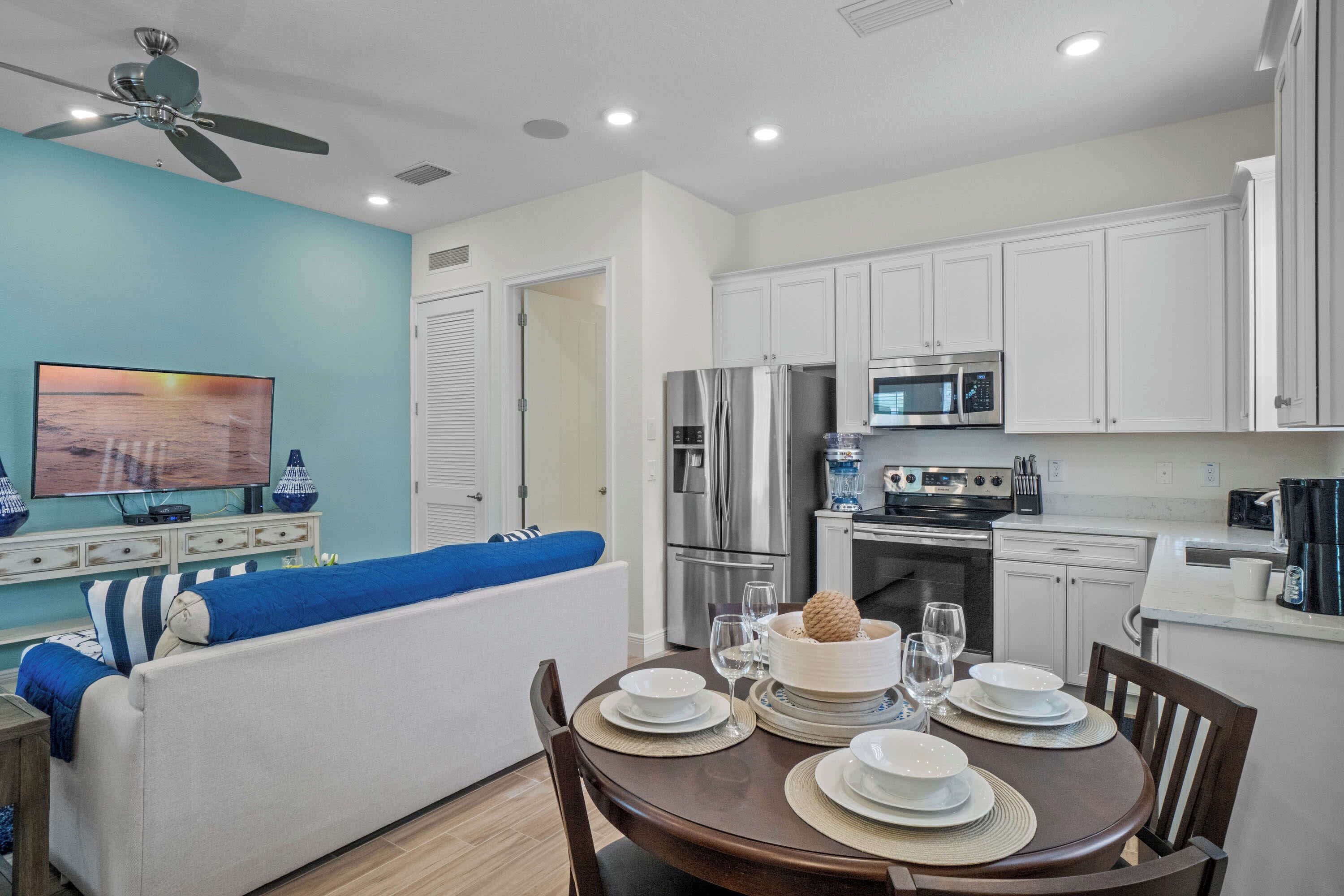Una cocina moderna con armarios blancos, electrodomésticos de acero inoxidable y un comedor con una mesa redonda preparada para cuatro comensales.
