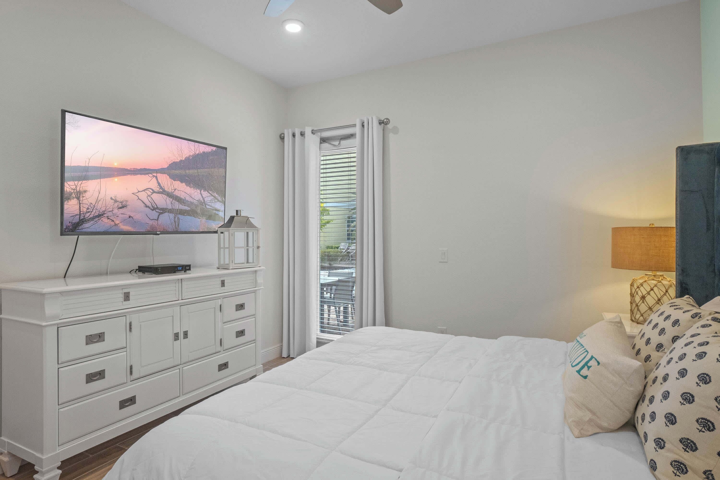 Une chambre à coucher avec un lit, un téléviseur fixé sur une commode et une fenêtre avec des rideaux.