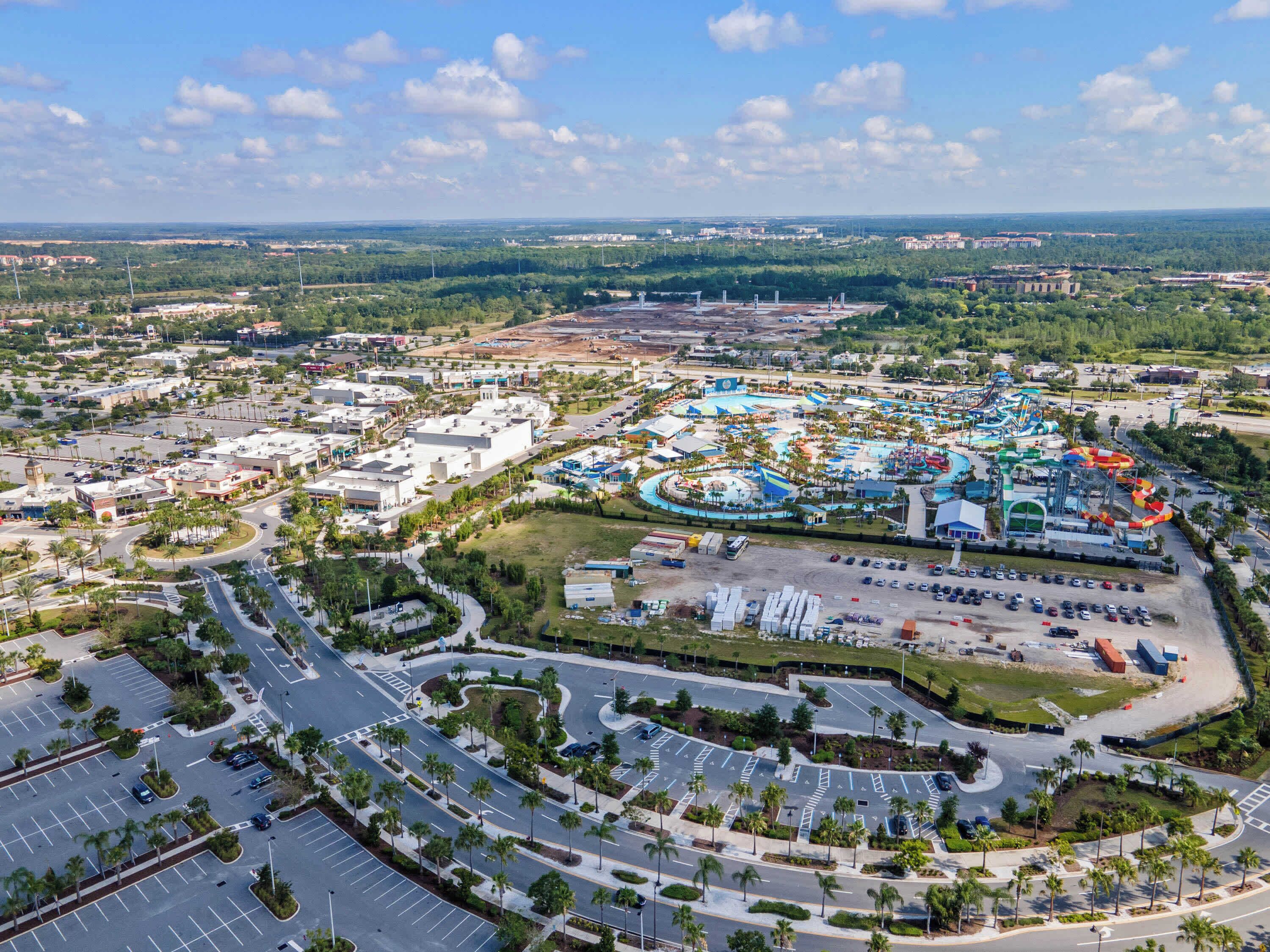 Vista aérea de un parque temático con diversas atracciones y espectáculos, rodeado de estacionamientos y carreteras.